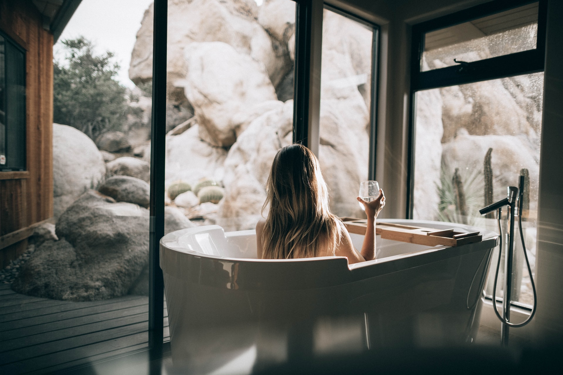 7 ways to have the best staycation ever - bring the spa to your home - woman sitting in bathtub holding a glass of wine looking out a natural rock formation