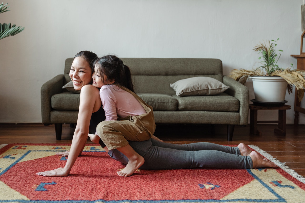 Mum doing a yoga stretch with daughter on top of her smiling