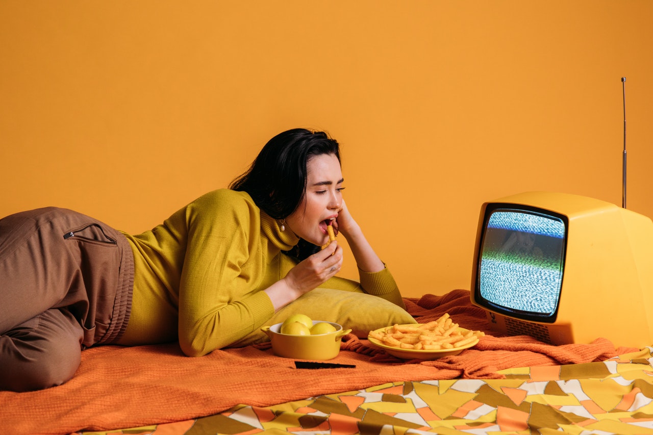woman-in-yellow-long-sleeve-shirt-watching-tv-and-eating